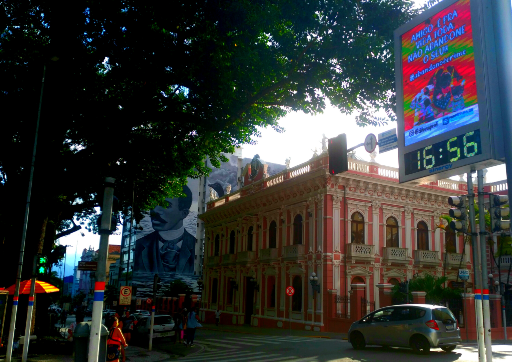 Palácio rosado - Museu Histórico de Santa Catarina dois homens caminhando no calçadão em frente ao museu e um homem com uma sdombinha. Faz sol por entre as