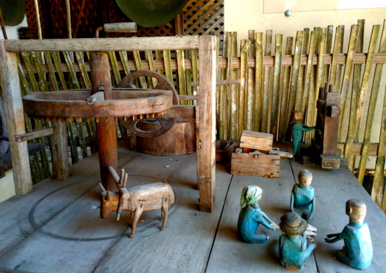 MIniatura da vida açoriana feita em madeira tem um boi, uma roda, e três crianças brincando sentadas com roupas azuis.